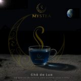 Xícara transparente com chá azul da marca Mystea sobre superfície semelhante ao solo lunar, com elementos gráficos dourados, o logotipo da Mystea e a Terra visível ao fundo em um cenário escuro estrelado.