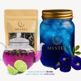 Pacote de flores secas de Clitoria ternatea da Mystea ao lado de um pote azul com gelo e uma chaleira transparente contendo chá roxo; limões frescos indicam a mudança de cor do chá ao adicionar acidez.
