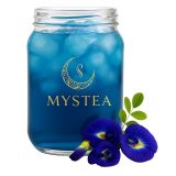 Pote de vidro transparente cheio de chá azul com gelo, estampado com o logo dourado da Mystea, ao lado de flores frescas de Clitoria ternatea e um pequeno ramo verde.