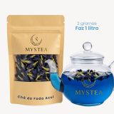Pacote do Chá da Fada Azul Mystea ao lado de uma chaleira de vidro contendo a infusão azul vibrante das flores Clitoria ternatea, com a indicação “2 gramas faz 1 litro”.